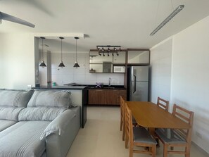 A modern kitchen with a dining area, a sofa, and a table with chairs. - 2 bedroom apartment, 1 suite, perfect location, new building, beachfront, downtown. (Mongaguá)
