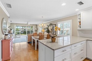 A spacious kitchen with a central island, a dining area with wicker chairs, and a view through the glass doors. - Whitney Hideaway 151 (Longboat Key)