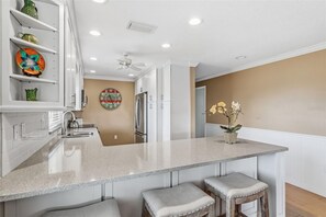 A kitchen with a central island, bar stools, a refrigerator, and a clock on the wall. - Whitney Hideaway 151 (Longboat Key)