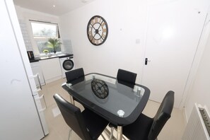 A modern kitchen with a dining table and chairs, a clock on the wall, and a window with a view of greenery. - Luxury 1-Bed, Free Parking, 15 Mins Central London, Sleeps 4 (London)