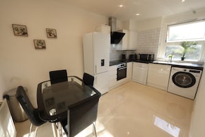 A modern kitchen with a dining table, chairs, a refrigerator, oven, microwave, and washing machine. - Luxury 1-Bed, Free Parking, 15 Mins Central London, Sleeps 4 (London)