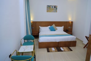 Habitación de hotel con una cama, mesitas de noche, una silla, una pequeña mesa y un cuadro en la pared.