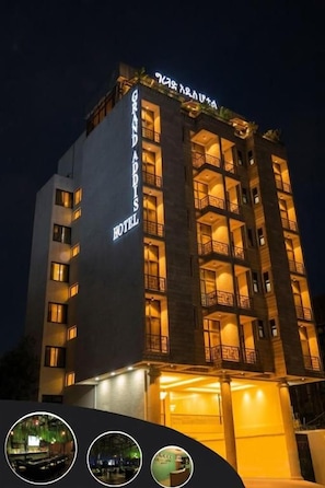 Een meerhoog hotel met verlichte reclame, balkons en een goed verlichte ingang.