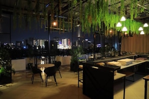 Een eetgedeelte binnen met tafels en stoelen, een bar en hangende planten.