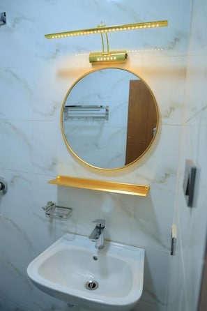 Een badkamer met een ronde spiegel, een wastafel en een verlichte spiegel boven de wastafel.