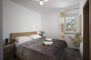 Ein Schlafzimmer mit Bett, Nachttisch, Lampe und einem Fenster mit Vorhängen.
