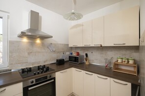 A modern kitchen with a gas stove, oven, microwave, and a hanging light fixture. - Villa Barbara and Brigita (Peruški)