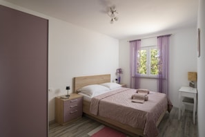 A bedroom with a bed, bedside table, lamp, and a window with curtains. - Villa Barbara and Brigita (Peruški)