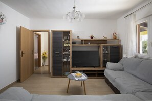 A modern living room with a sofa, a coffee table, a TV, and a wooden cabinet with glass doors. - Villa Barbara and Brigita (Peruški)