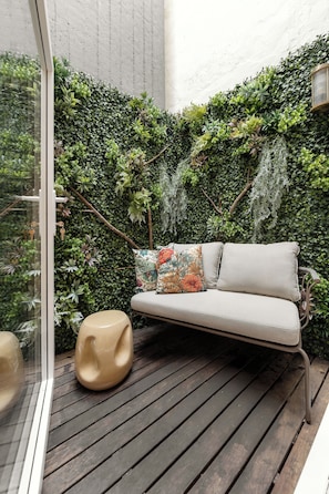 A cozy outdoor seating area with a cushioned bench and a unique stool, surrounded by lush greenery. - NEW: Bloom Porto | Luxury Clérigos Gem with Patio (Unknown)