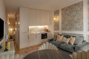 A modern living room with a grey sofa, a coffee table, and a kitchen area with white cabinets and a marble backsplash. - NEW: Bloom Porto | Luxury Clérigos Gem with Patio (Unknown)