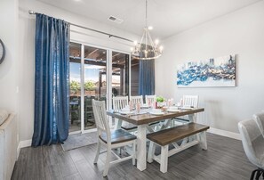 Espaço de refeições com mesa posta para quatro pessoas, cadeiras brancas, um banco e um lustre.