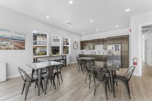 Eine moderne Küche mit Edelstahlgeräten, ein Essbereich mit Glastischen und Metallstühlen sowie ein großes Gemälde an der Wand.
