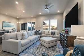 A modern living room with a sectional sofa, ottoman, and a ceiling fan. - Snow Canyon Poolhouse 8 Bedroom Home (Santa Clara)