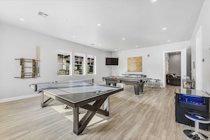 Una habitación amplia con una mesa de ping pong, dos mesas de fútbol de mesa y una mesa de fútbol de mesa con base azul.