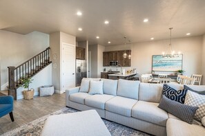 Ein modernes Wohnzimmer mit grauem Sofa, einem Essbereich mit weißem Tisch und einer Küche mit Holzschränken.