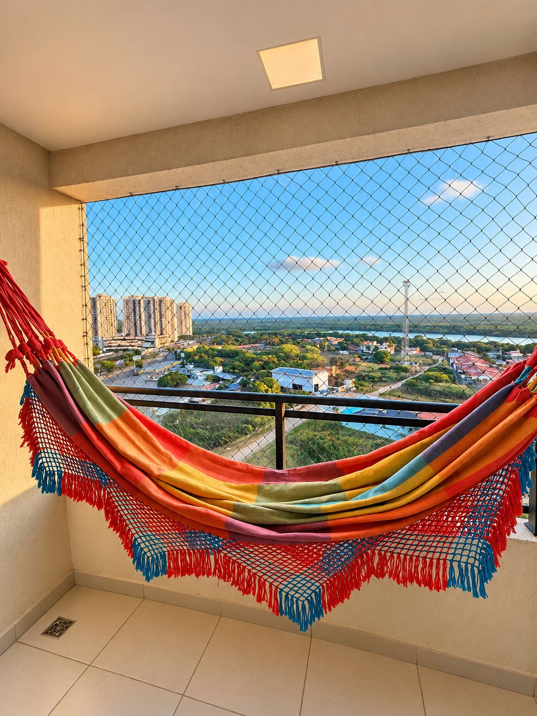 A balcony with a hammock, a view of a cityscape, and a clear sky.