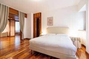 A bedroom with a large bed, wooden flooring, a door leading to another room, and a bedside table with a lamp. - Residenza Adua - 100mt dall'Arena  (Verona)