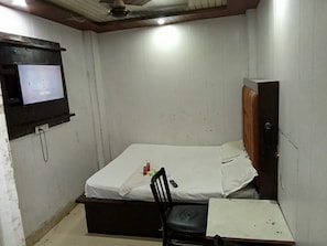 Een kleine kamer met een enkel bed, een televisie aan de muur, een stoel en een klein tafeltje.