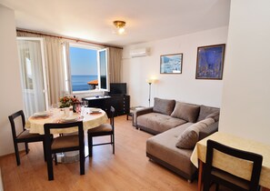 A furnished living room with a dining area, a sofa, a TV, and a view of the sea. - Adorable 1-bedroom apartment with AC, beautiful sea view in charming Dubrovnik (Dubrovnik)