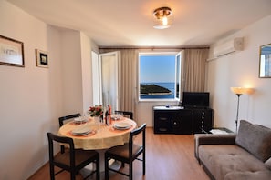 A dining area with a table set for four, a sofa, a television, and a window with a view of the sea. - Adorable 1-bedroom apartment with AC, beautiful sea view in charming Dubrovnik (Dubrovnik)