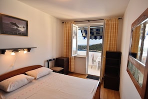 Ett hotellrum med en säng, en stol, ett skrivbord, ett fönster med gardiner och utsikt över havet.