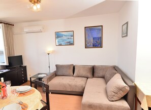 A living room with a sofa, a flat-screen TV, a dining table with chairs, and two framed paintings on the wall. - Adorable 1-bedroom apartment with AC, beautiful sea view in charming Dubrovnik (Dubrovnik)