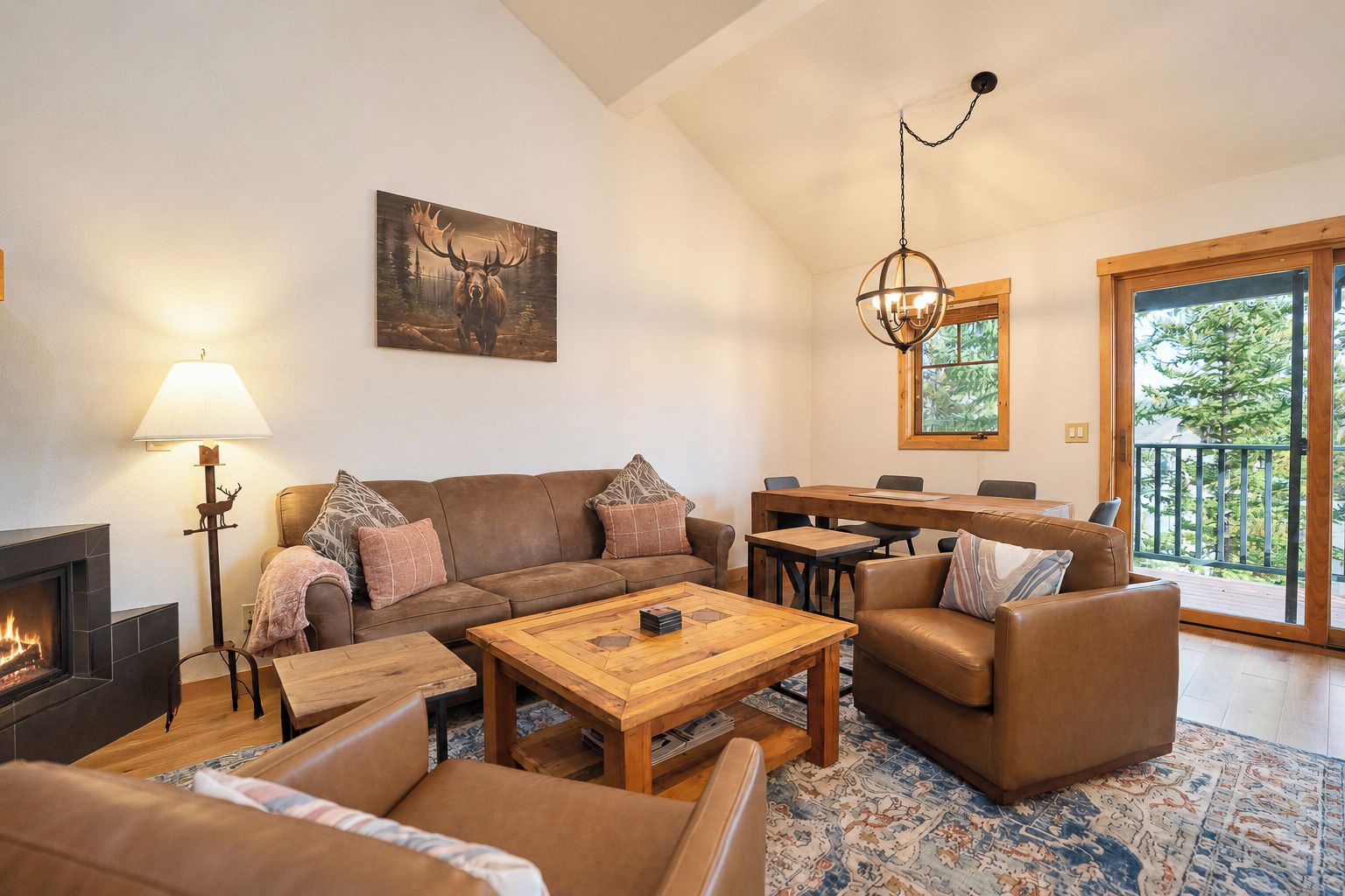 A cozy living room with a fireplace, a dining area, and a large window with a view of trees.