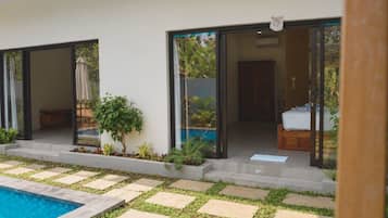 Un espace piscine extérieur moderne, doté d’une entrée avec porte vitrée, d’un petit jardin agrémenté de pas japonais et d’un banc en bois.