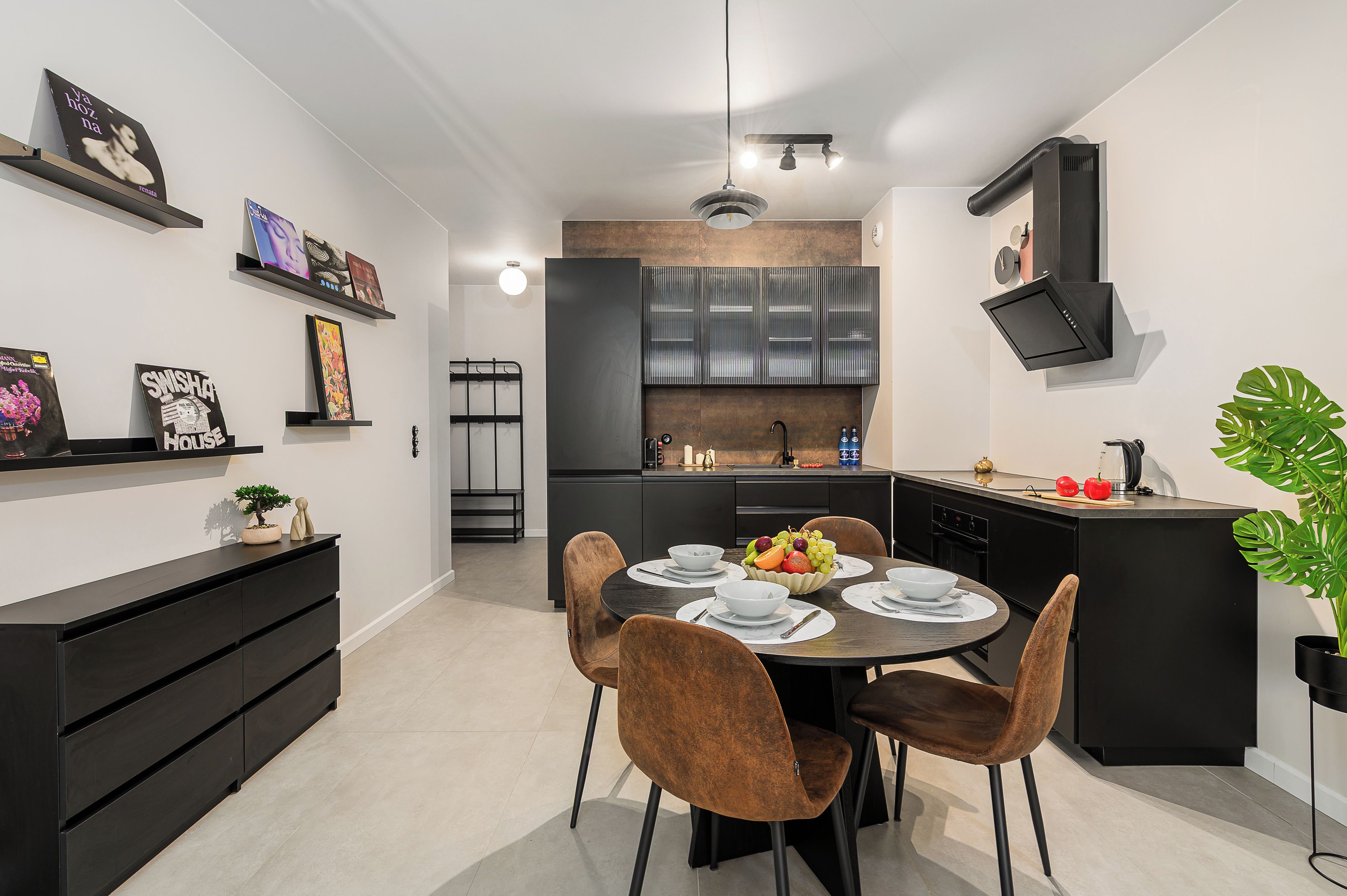 A modern kitchen with a dining area, featuring a round table with chairs, a built-in oven, and a black cabinet with a TV mounted above it.