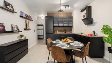 A modern kitchen with a dining area, featuring a round table with chairs, a built-in oven, and a black cabinet with a TV mounted above it.
