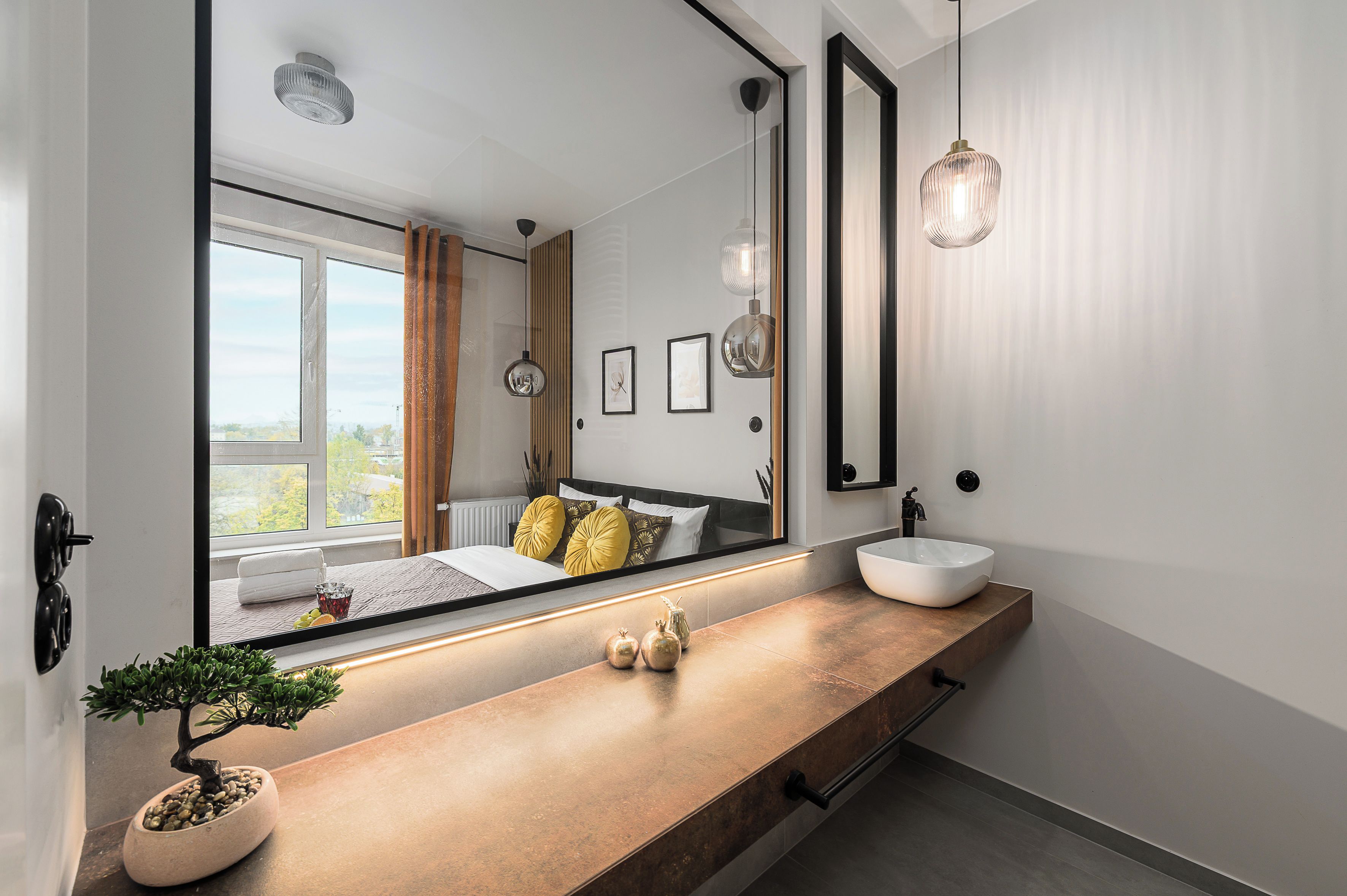 A modern bathroom with a large mirror, a wooden vanity, a round sink, and a potted plant.