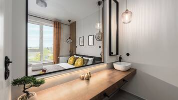 A modern bathroom with a large mirror, a wooden vanity, a round sink, and a potted plant.