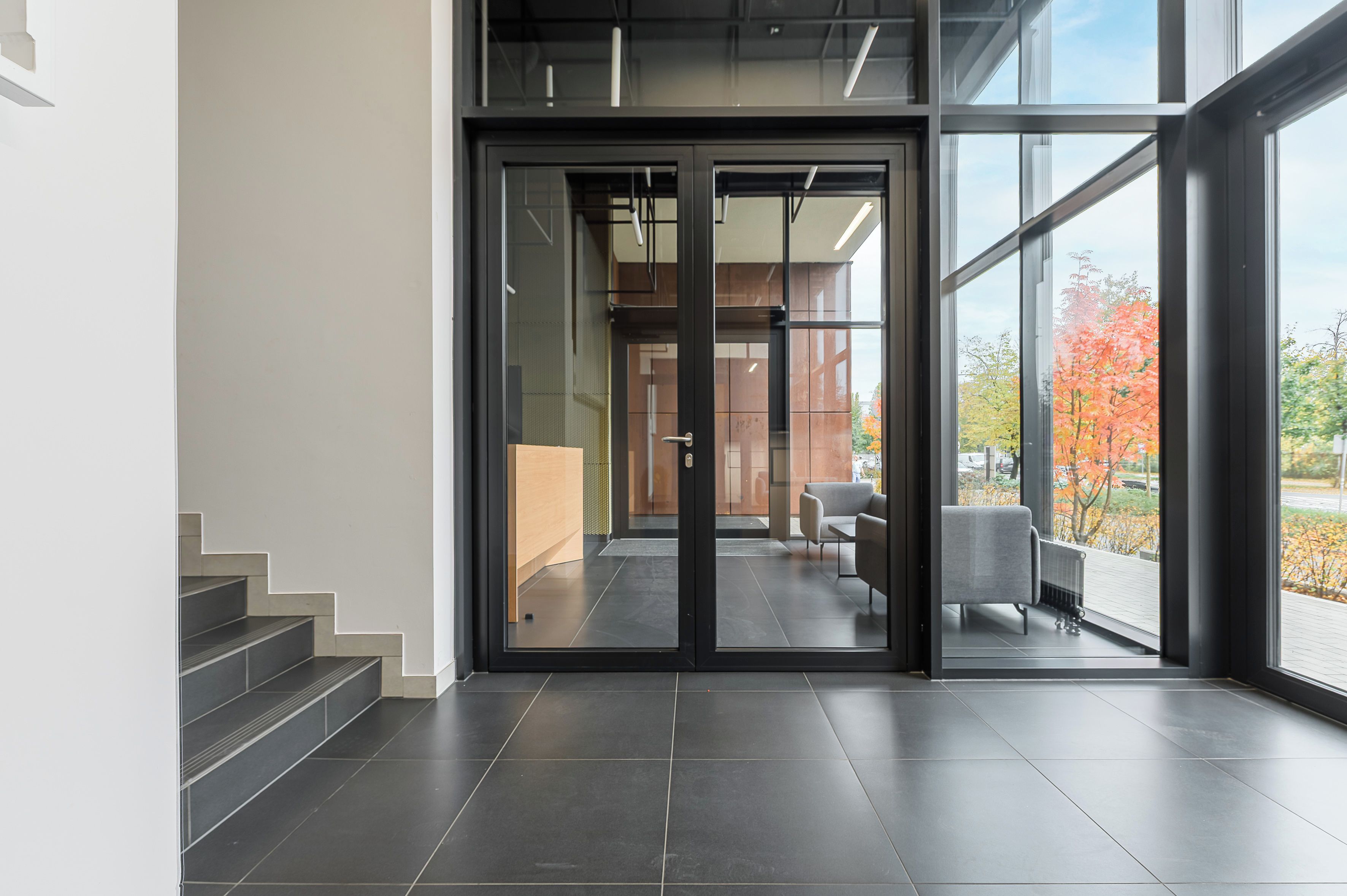 Un intérieur moderne avec une porte vitrée donnant sur un espace salon, un escalier et une vue sur le feuillage automnal.