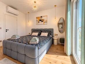 Un dormitori modern amb un llit gran, una taula de nit, un mirall i una lluminària de sostre.