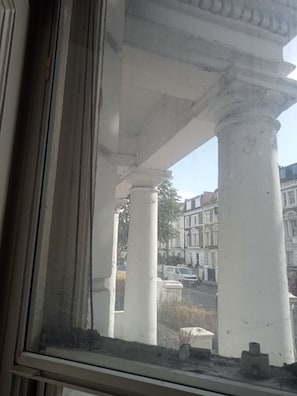 A view through a window with a view of white columns and a street with buildings. - Short term stay available in 1 bed flat (London)