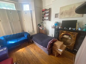 A bedroom with a bed, a blue sofa, a dresser, a mirror, and a fireplace. - Short term stay available in 1 bed flat (London)