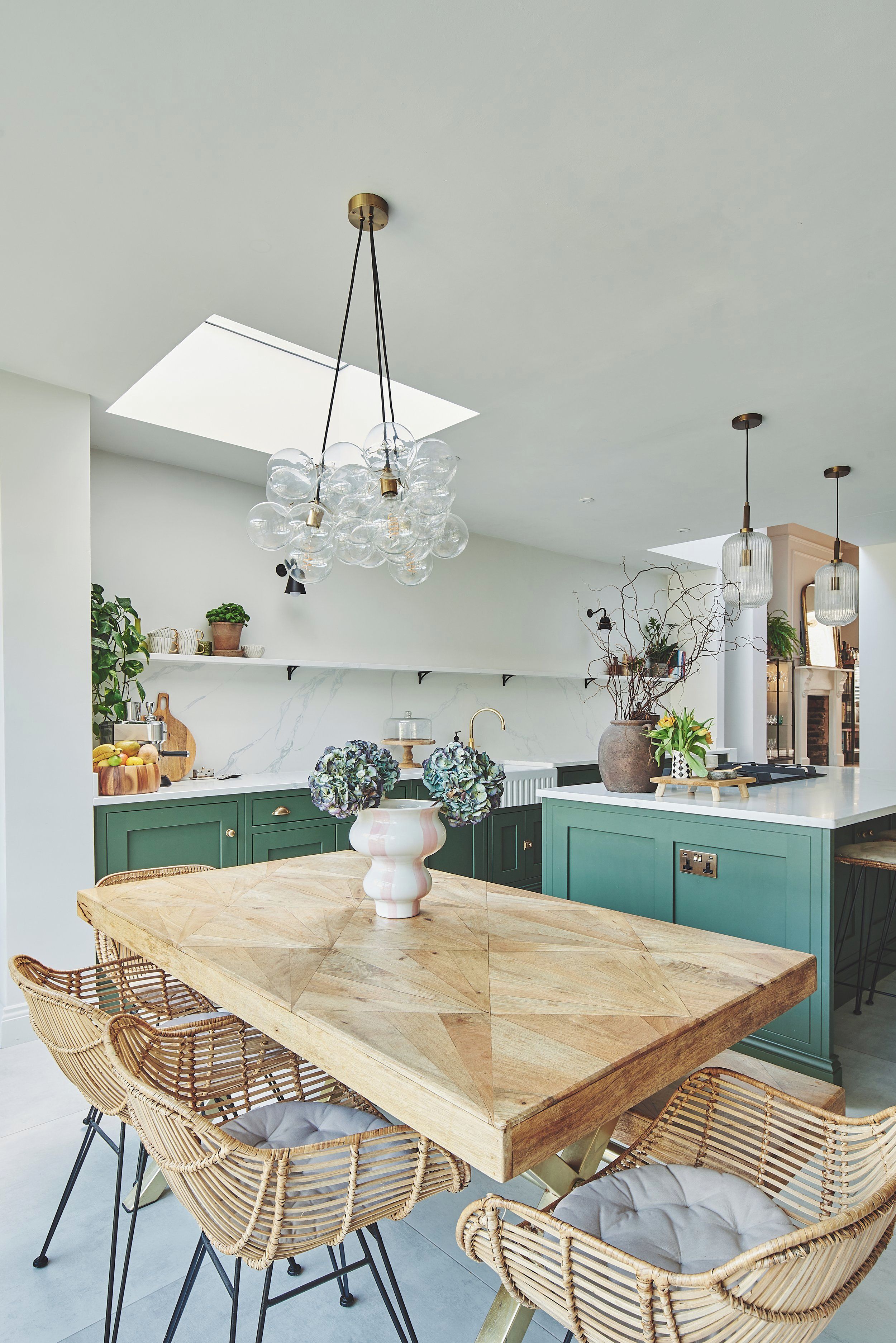 A modern kitchen with a central island, pendant lighting, and wicker chairs.
