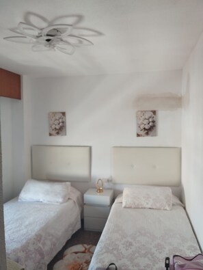 A bedroom with two beds, a nightstand, and a ceiling fan. - The El Tiburon vacation rental is located 70 meters from the beach and the Maritim Passeig. (Grau i Platja)
