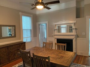 A dining area with a wooden herringbone table, four chairs, a ceiling fan, and a fireplace with a white mantel. - That big blue house downtown! (Wilmington)