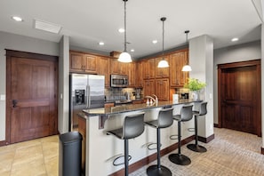 A modern kitchen with wooden cabinets, stainless steel appliances, and a bar area with stools. - New Listing! Riverstone Condo | Private Balcony | Walk to Shops and Dining (Coeur d'Alene)