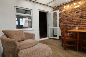 A room with a brick wall, a white door, a wooden dining table with chairs, and a brown upholstered chair. - Lincolnshire wolds cottage - private garden - games room - 30 mins from Lincoln (Ludford)