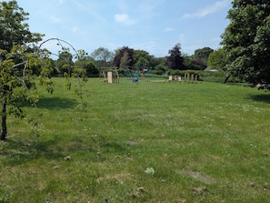 Ein grünes Freigelände mit Schaukeln und Holzspielgeräten.