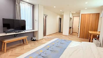 A hotel room with a bed, a TV on a stand, a wooden bench, a desk, and a wardrobe.
