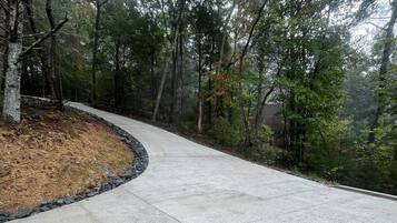 A paved pathway curving through a wooded area with a wooden fence on one side.