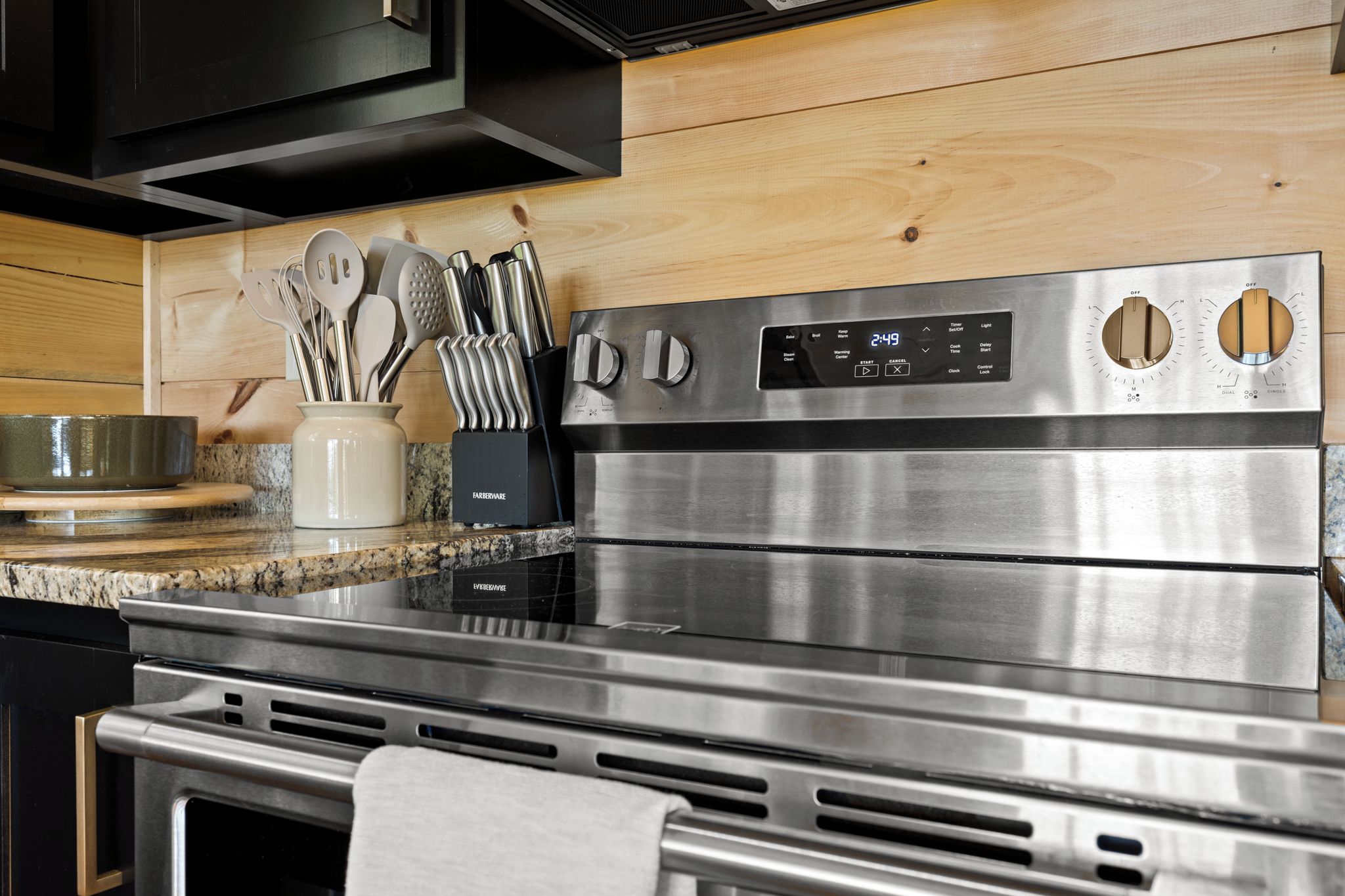 Una cocina de acero inoxidable con encimera de granito, un bloque de cuchillos Farberware y un horno de acero inoxidable.