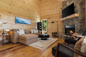 Un interior de cabaña acogedor con chimenea, paredes de madera, un sofá, una mesa de centro y un televisor.