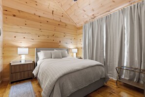 Un dormitorio con paneles de madera, una cama, mesitas de noche y un ventanal con cortinas.