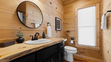 Une salle de bain rustique, avec des murs en bois, un meuble-lavabo en bois, deux vasques, des toilettes, un miroir et une fenêtre.