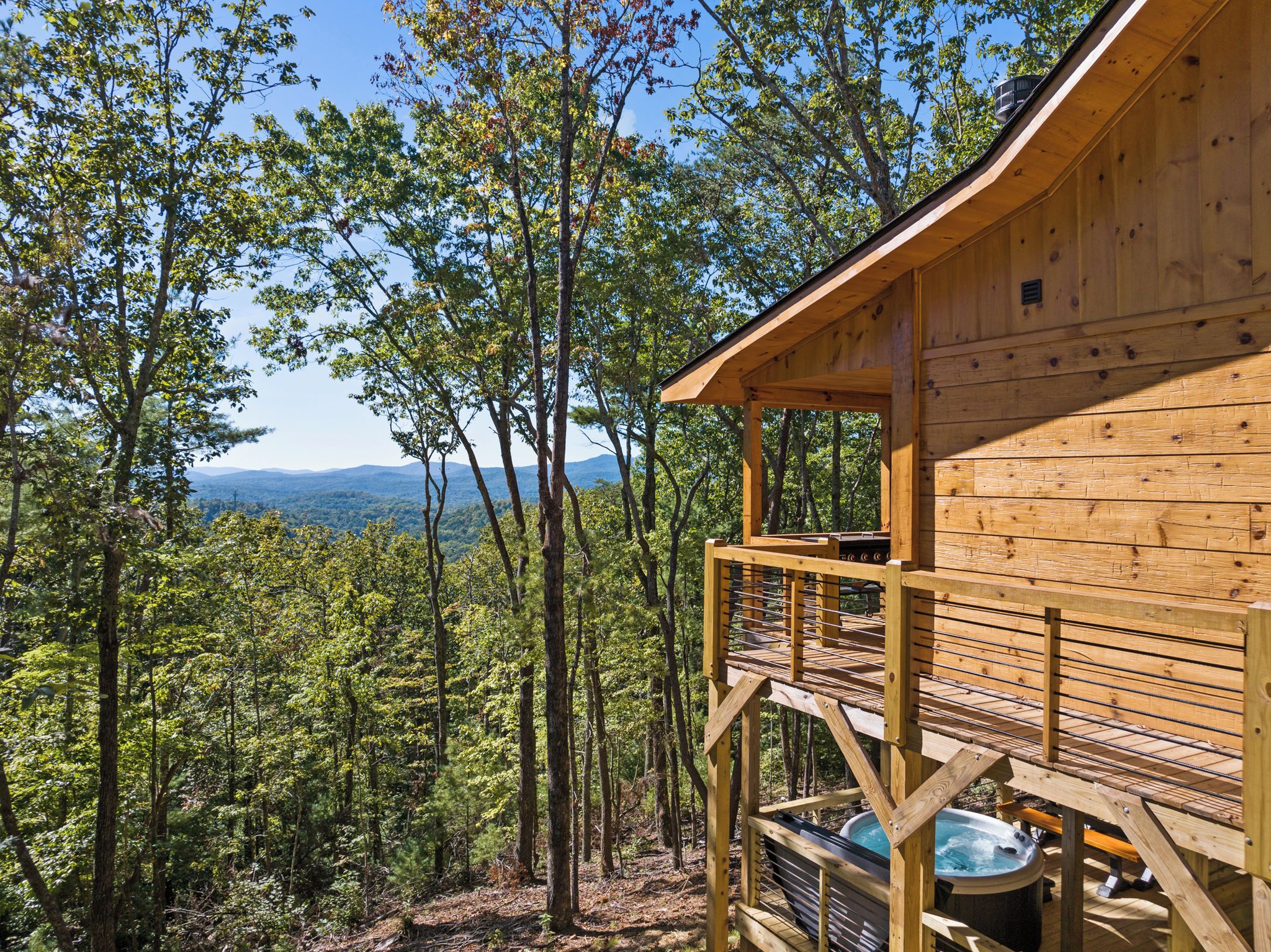 Una cabaña de madera con terraza y vistas a un bosque y montañas distantes.